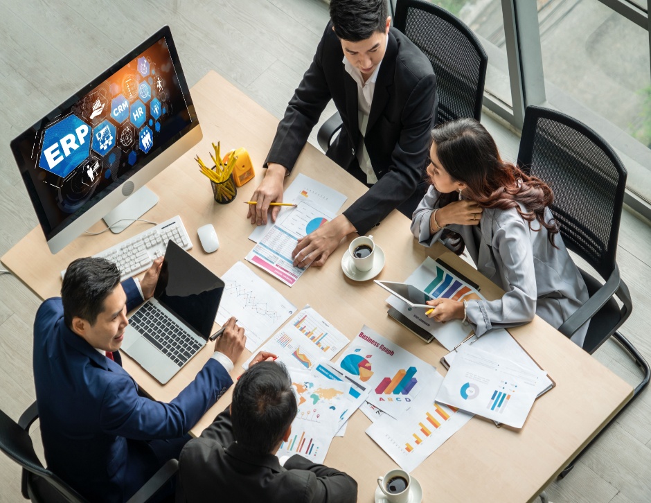 Description: Accounting team of men and women collaborating on ERP planning at desk with computer to analyze performance and create reports for operations management.